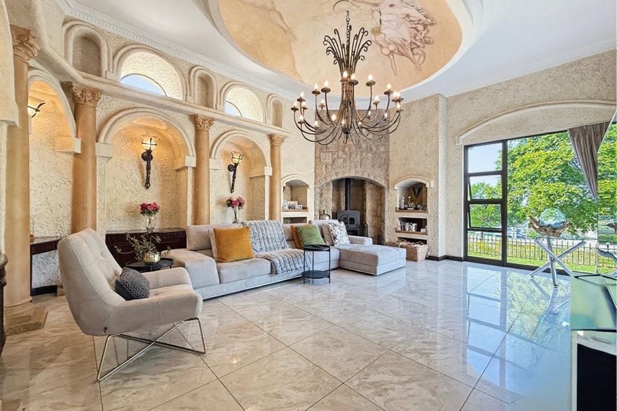 Spacious living room featuring a dramatic ceiling mural, stone fireplace, ornate wall niches with decorative columns, and polished marble flooring with garden access.