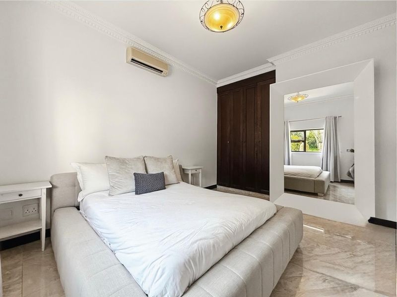 A well-maintained bedroom featuring tiled flooring, crown molding, built-in dark wood cupboards, and a wall-mounted air conditioning unit.