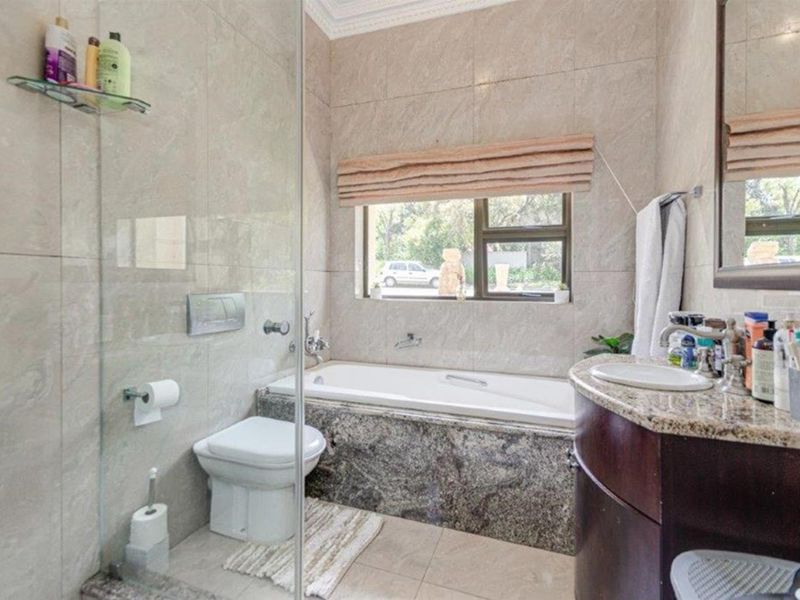 A well-appointed bathroom featuring a built-in bathtub, granite-topped vanity, wall-mounted toilet, and a glass-enclosed shower with neutral wall tiling.
