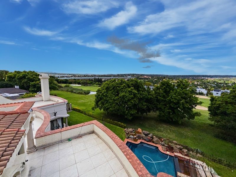 Elevated view overlooking a swimming pool, terrace, and expansive green landscape with a distant bridge.