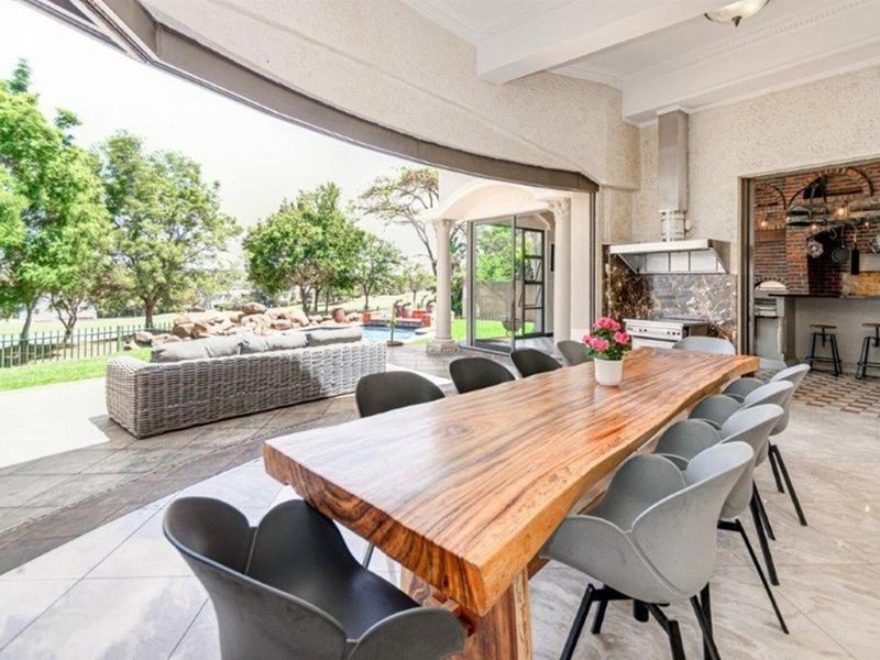 Spacious covered patio featuring a built-in braai, stone tile flooring, and seamless flow to the outdoor garden and pool area through large sliding doors.