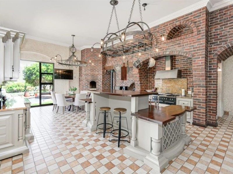Spacious open-plan kitchen and dining area featuring a rustic brick fireplace, custom cabinetry, a central island, and elegant chandelier lighting.