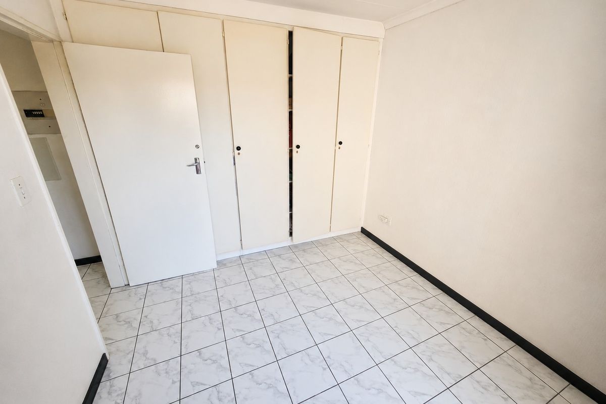 A clean, empty bedroom featuring neutral tiled flooring and ample built-in cupboard storage space.