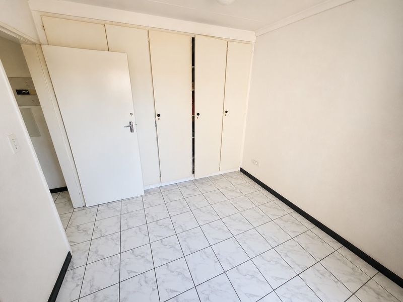 A clean, empty bedroom featuring neutral tiled flooring and ample built-in cupboard storage space.