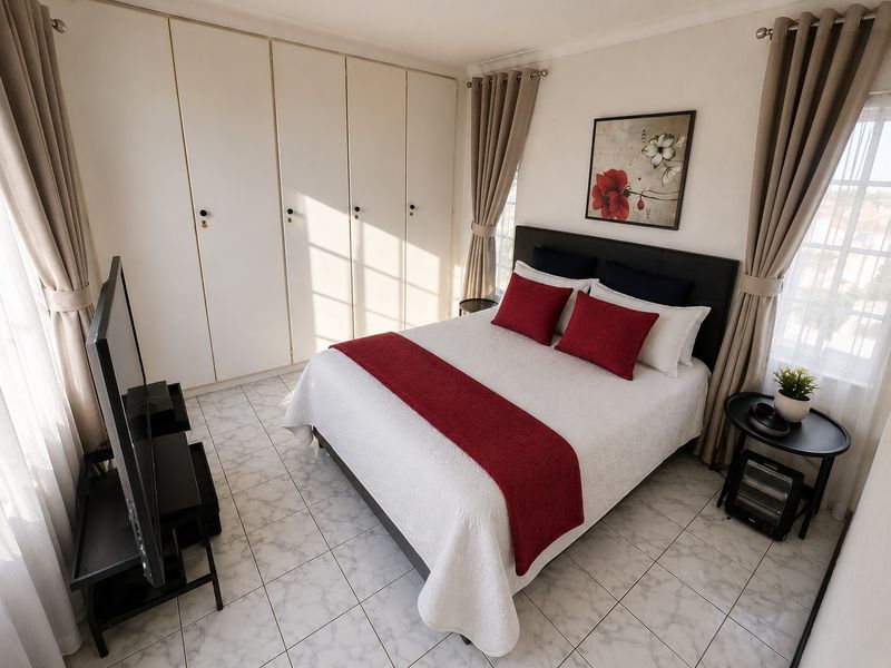 A well-maintained bedroom featuring built-in cupboards, tiled flooring, and dual windows with curtain rails, offering a bright and functional living space.