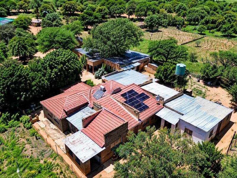 Aerial view of a farm property featuring multiple structures with a mix of tiled and corrugated metal roofing, solar panels, and a water tank.