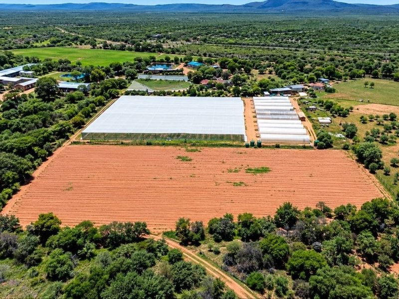Aerial view of a farm property featuring extensive greenhouse structures, agricultural tunnels, cultivated fields, and water storage infrastructure set within a rural landscape.