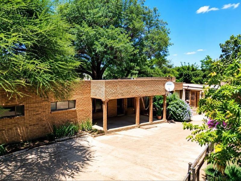 Front view of a face brick farm-style residence featuring a covered patio, paved driveway, and established garden surroundings.