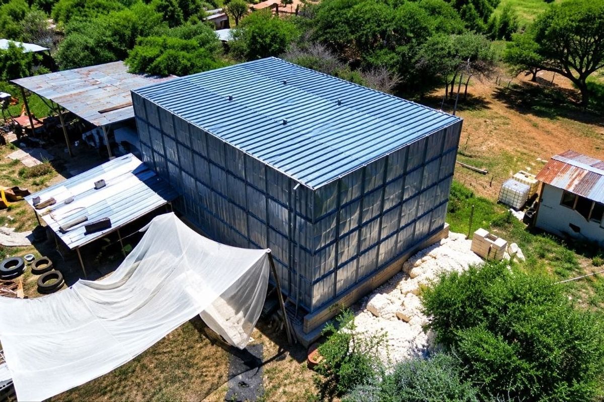 Aerial view of a farm property featuring a large metal water storage tank, an open-sided shed, and a small outbuilding set within a rural landscape.