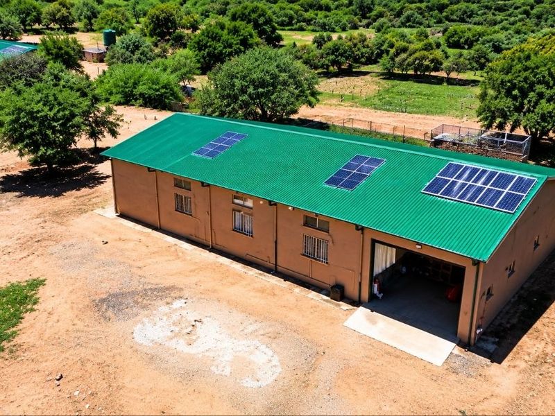 Aerial view of a farm outbuilding featuring a green corrugated metal roof with integrated solar panels and security-barred windows.