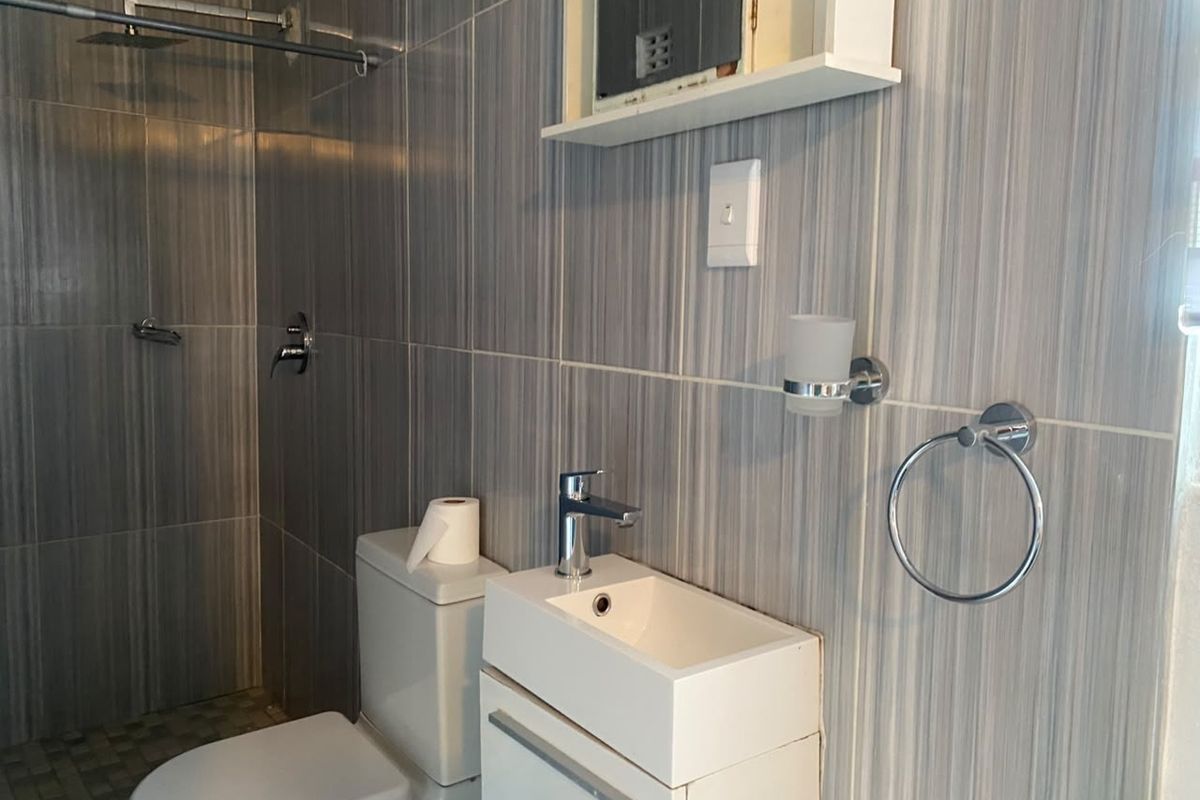 A compact bathroom featuring modern grey wall tiles, a built-in vanity with a basin, a toilet, and a walk-in shower area.