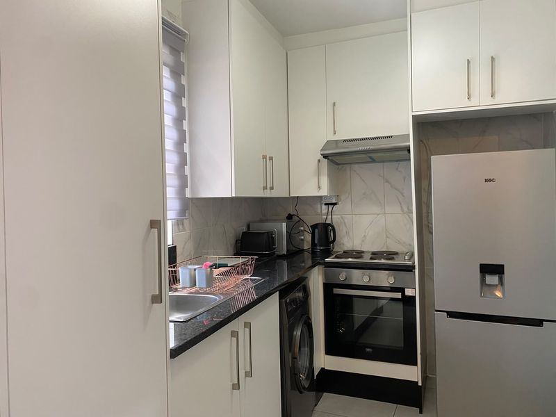A compact, modern kitchen featuring white cabinetry, granite countertops, a tiled backsplash, and built-in stainless steel appliances.