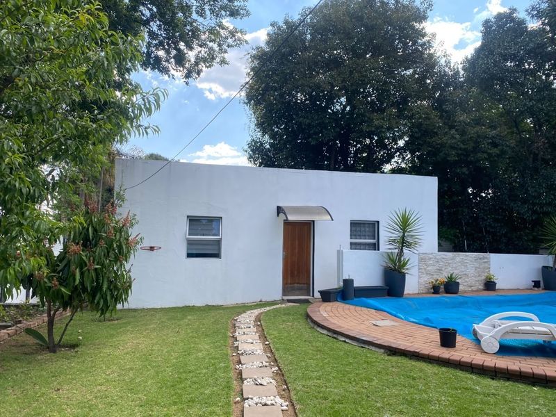 Rear exterior view featuring a swimming pool with a blue cover, a stone-clad feature wall, and a paved garden path leading to the building entrance.