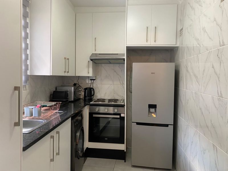 A compact, modern kitchen featuring white cabinetry, granite countertops, marble-look tiled walls, and integrated appliances including an oven and hob.