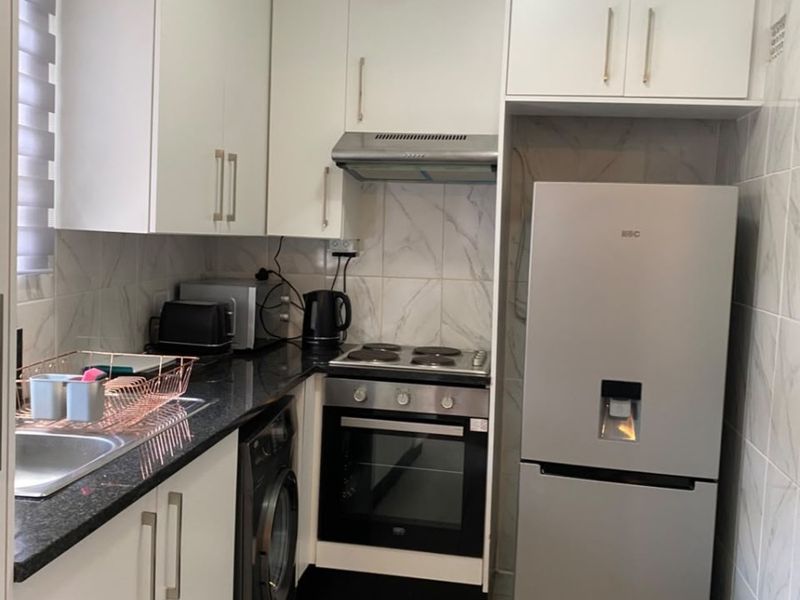 A compact, modern kitchen featuring white cabinetry, granite countertops, stainless steel appliances, and tiled finishes throughout.
