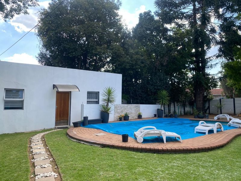 Outdoor pool area featuring a swimming pool with a blue cover, brick coping, stone feature wall, and a landscaped garden path.