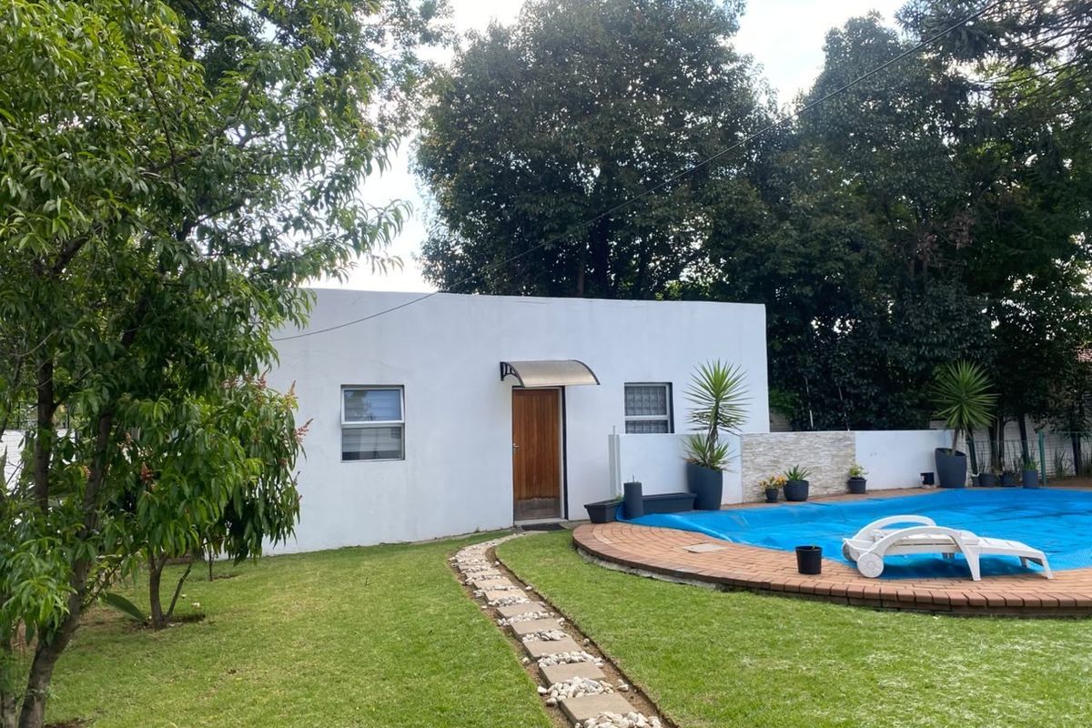 A well-maintained rear garden featuring a swimming pool with a cover, a stone pathway, and a clean exterior building facade.