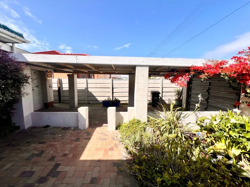 A covered outdoor patio area featuring paved flooring, concrete structural pillars, and a secure boundary wall, offering potential for an outdoor entertainment space.