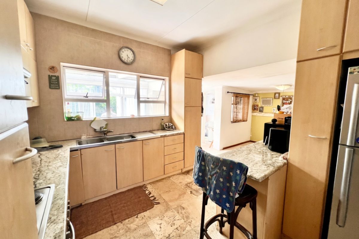 A functional kitchen featuring light wood cabinetry, stone countertops, a double basin sink, and a breakfast bar, with tiled flooring and backsplash.