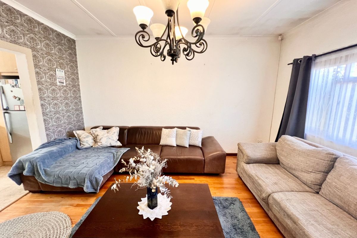 A comfortable living room featuring hardwood flooring, a decorative chandelier, and a textured wallpaper feature wall, providing a warm and inviting atmosphere.