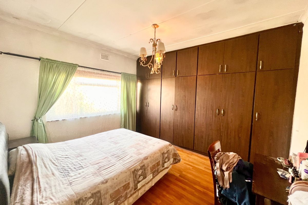A bedroom featuring extensive built-in wooden cupboards, laminate flooring, and a classic chandelier, offering ample storage space.