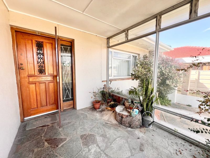 An enclosed front patio featuring stone paved flooring, a classic timber entrance door with decorative metal detailing, and large glass panels.