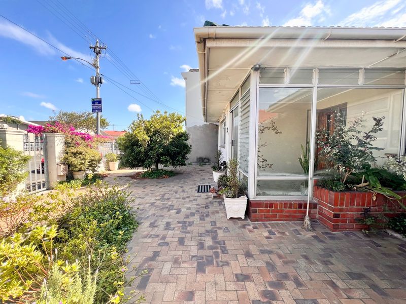 A paved outdoor patio area featuring a glass-enclosed sunroom and built-in brick planter boxes, providing a functional transition space between the garden and home.