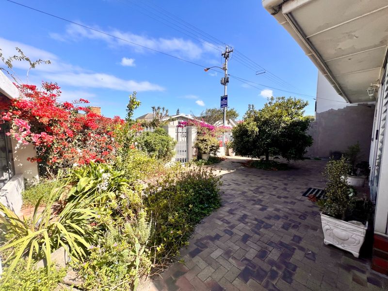 A paved outdoor patio area featuring a covered veranda, established garden beds, and a secure boundary wall with a gate.