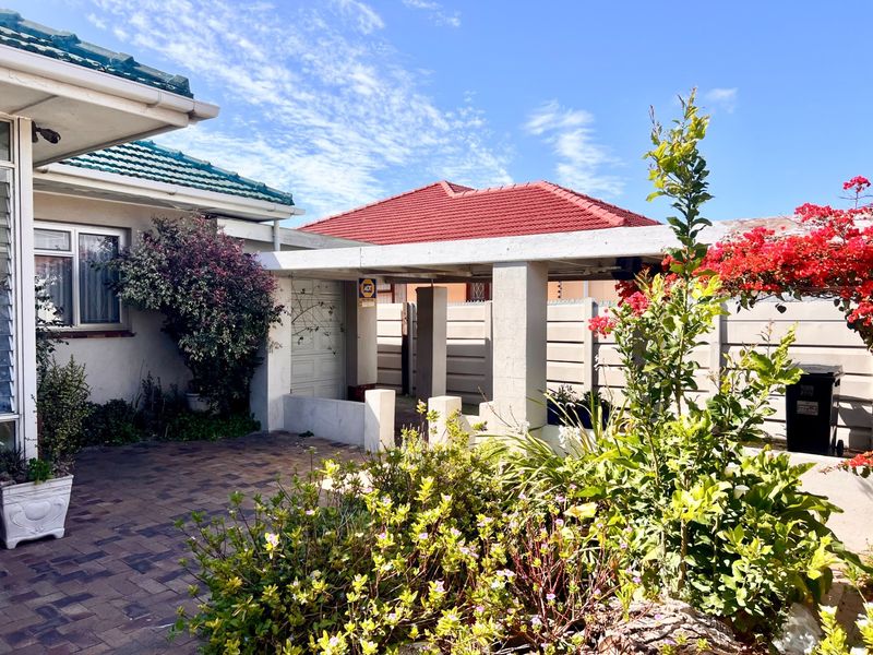 Front exterior view featuring a paved driveway, a covered carport, and a secure boundary wall with established garden landscaping.