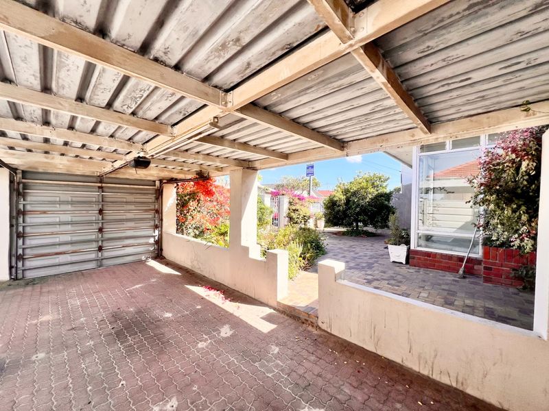 A covered outdoor patio area featuring a corrugated metal roof, paved flooring, and a low masonry wall, providing a functional transition space.