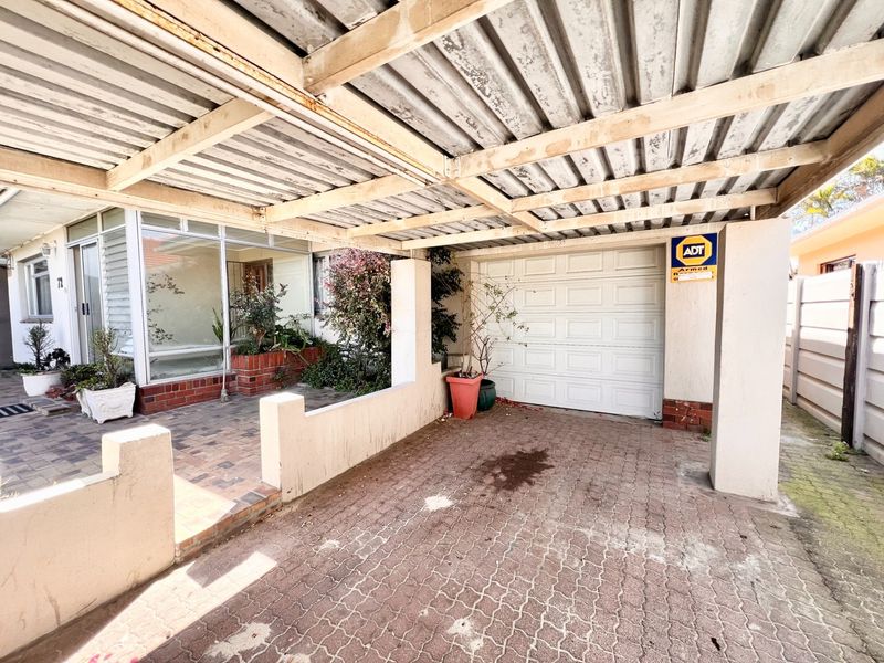 A covered carport area featuring a paved driveway, a single garage door, and integrated security signage, providing sheltered off-street parking.
