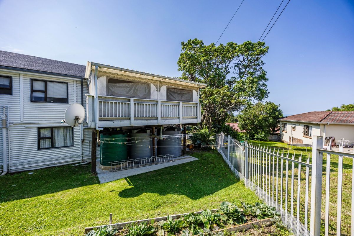 Rear view of the property featuring a raised deck, water storage tanks, and a fenced garden area with established lawn.