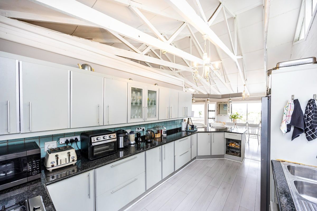 Spacious kitchen featuring light-toned cabinetry, granite countertops, a tiled backsplash, and striking exposed white roof trusses, creating an airy and open atmosphere.