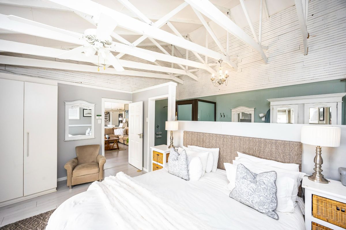 Spacious bedroom featuring high vaulted ceilings with exposed white timber trusses, laminate flooring, and convenient access to an adjoining en-suite bathroom.