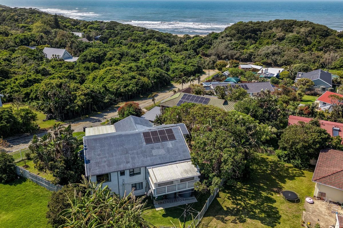 Aerial view of the property showing the roof structure with solar panels, a covered rear patio, and surrounding coastal landscape.