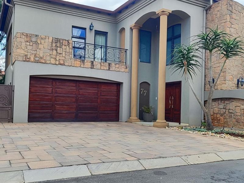 A well-maintained double-storey residence featuring stone cladding, a paved driveway, a double garage, and an elegant entrance with decorative columns.