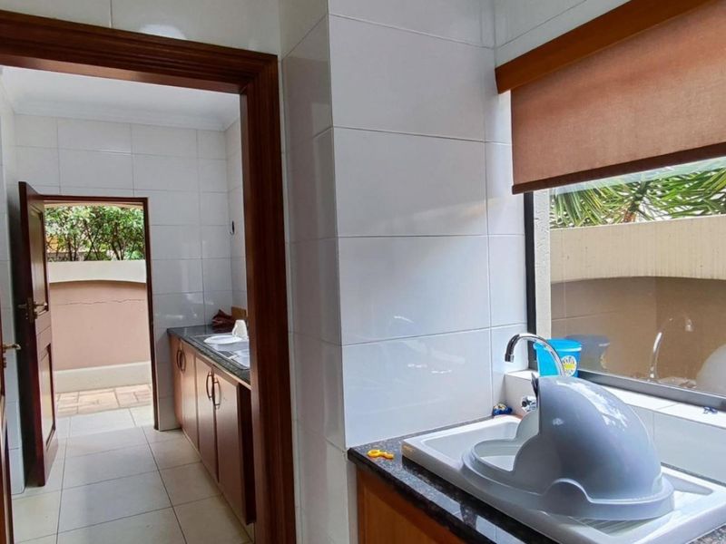 A functional scullery area featuring built-in cabinetry, granite countertops, and a stainless steel sink, with direct access to an outdoor space.
