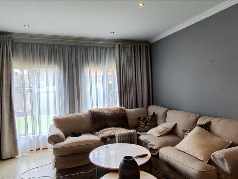 A comfortable living room featuring tiled flooring, recessed downlighting, and large windows with floor-to-ceiling curtains, creating a bright and inviting space.