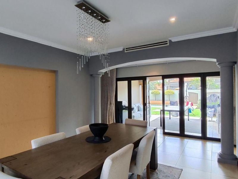 Dining room featuring tiled floors, decorative columns, and sliding glass doors leading to the patio, with an unfinished wall section requiring attention.