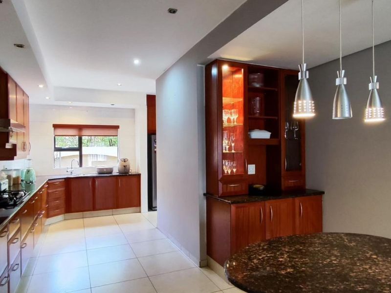 Spacious kitchen featuring warm wood cabinetry, granite countertops, built-in appliances, and a dedicated dining nook with elegant pendant lighting.