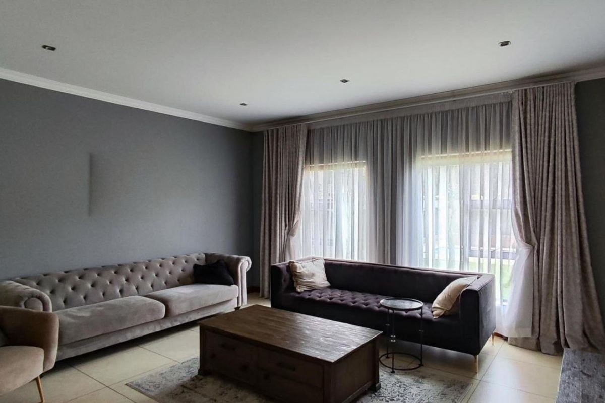A well-maintained living room featuring neutral tiled flooring, recessed downlighting, and elegant floor-to-ceiling curtains.