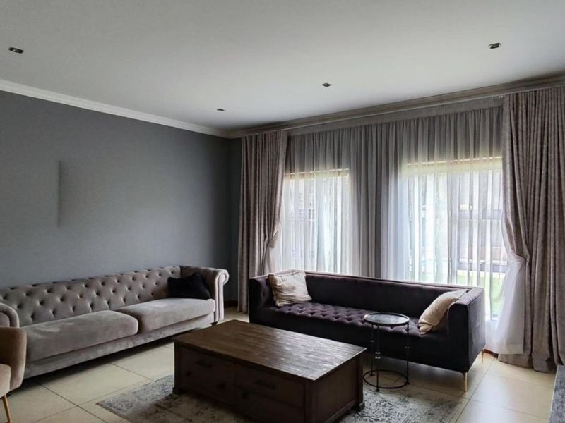A well-maintained living room featuring neutral tiled flooring, recessed downlighting, and elegant floor-to-ceiling curtains.