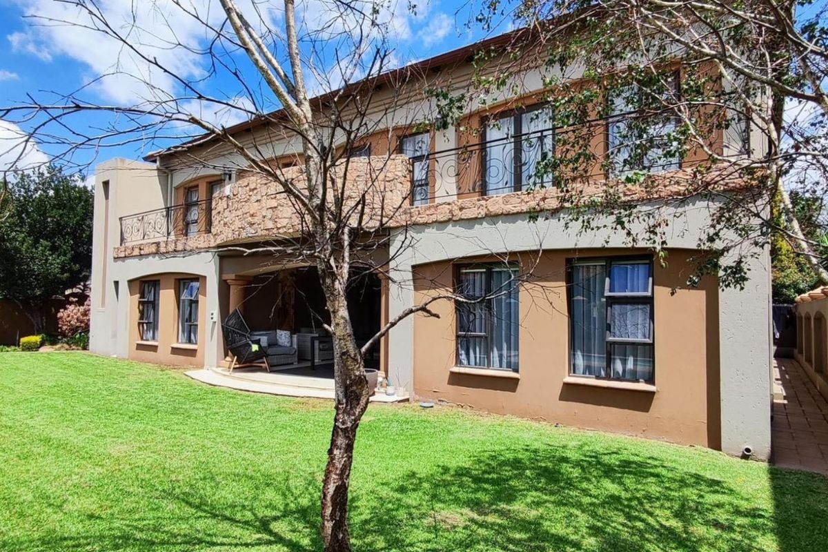 Rear elevation of a double-storey house featuring stone cladding, a balcony with wrought iron railings, and a covered patio overlooking a landscaped garden.