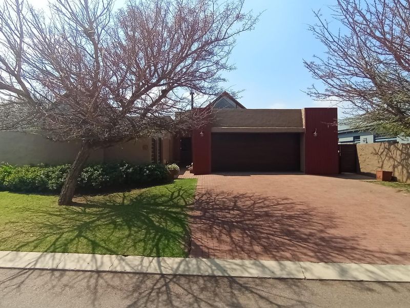 Front elevation of the property featuring a paved driveway, double garage, and established garden with boundary walling.