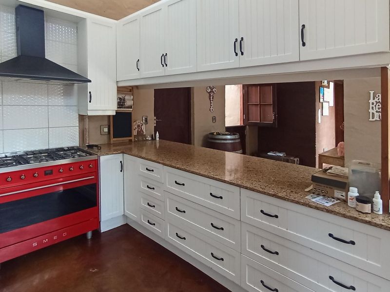 Kitchen featuring white cabinetry, granite countertops, and a prominent red Smeg gas range, with a pass-through window overlooking the adjacent living area.