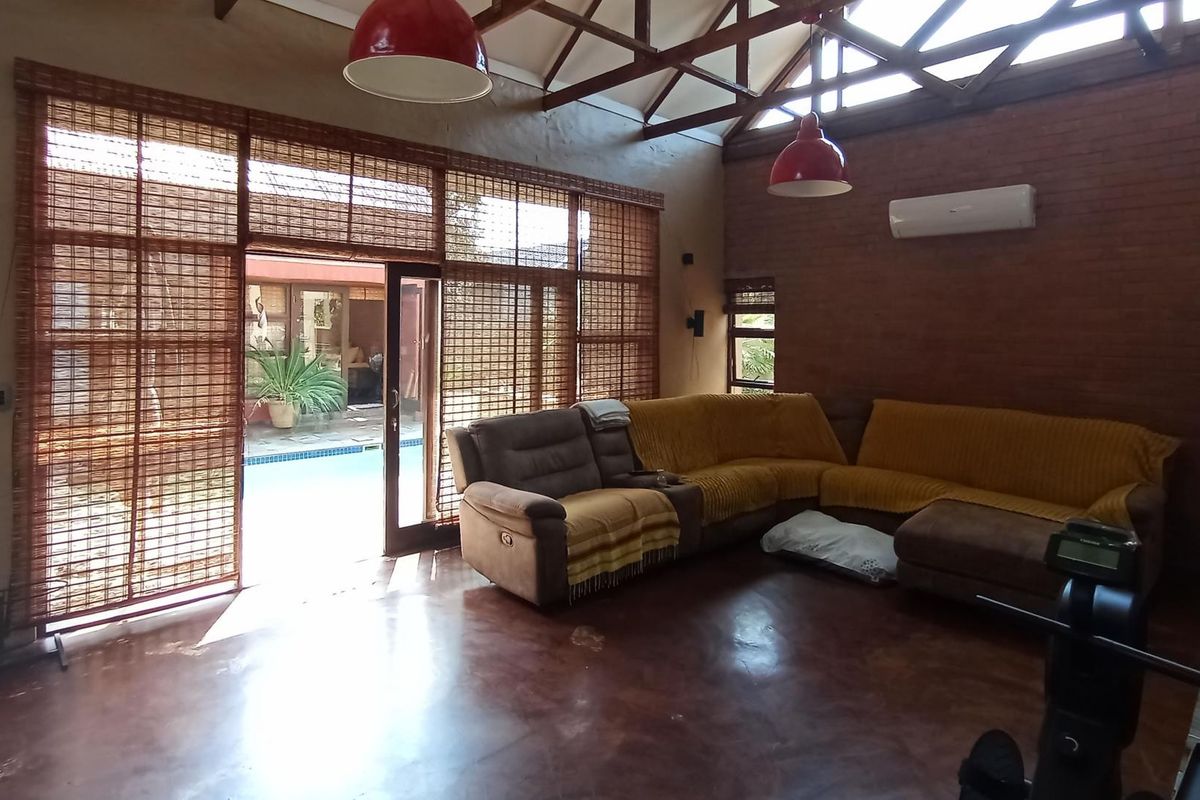 Spacious living room featuring exposed brick walls, polished concrete floors, and high vaulted ceilings with timber trusses, opening directly onto a patio area.