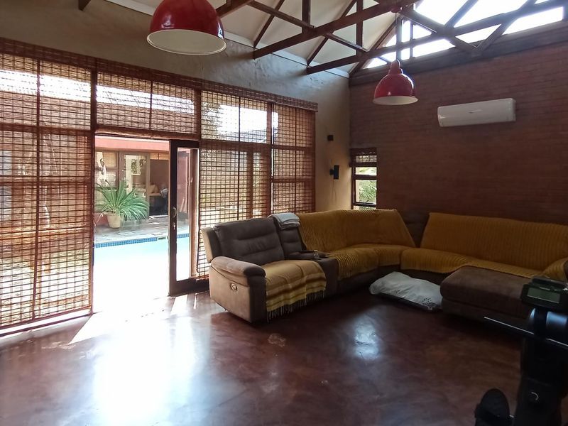 Spacious living room featuring exposed brick walls, polished concrete floors, and high vaulted ceilings with timber trusses, opening directly onto a patio area.