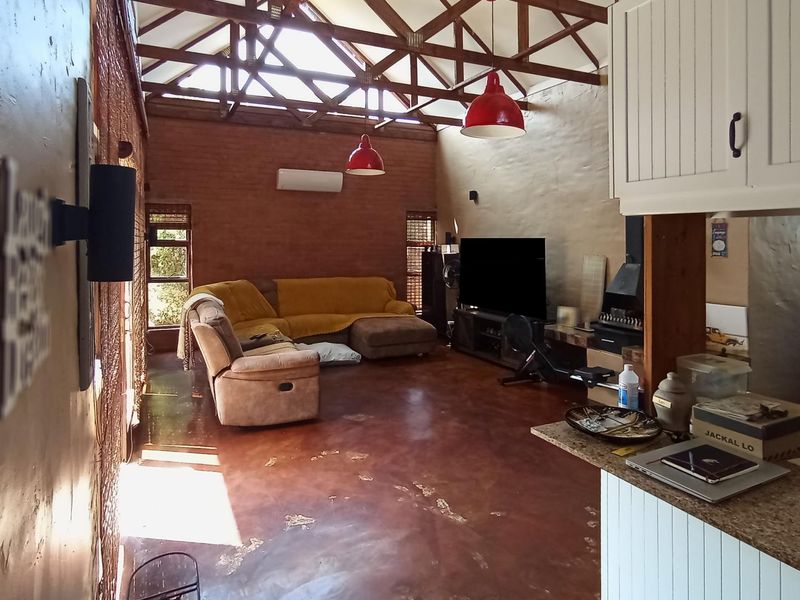 Spacious open-plan living area featuring exposed brick walls, high vaulted ceilings with timber trusses, polished concrete floors, and a built-in fireplace.