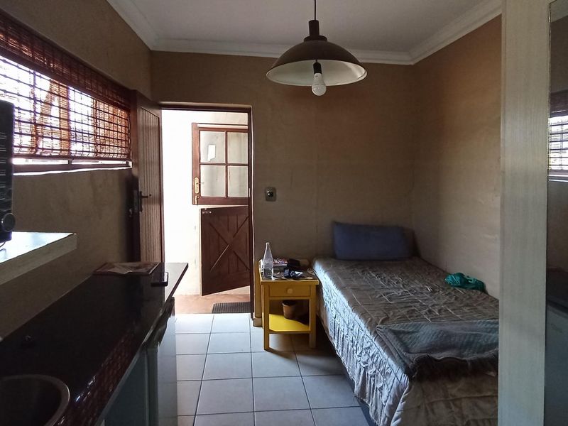 A compact open-plan living space featuring a kitchenette area with a sink and tiled flooring, leading directly to an exterior door.