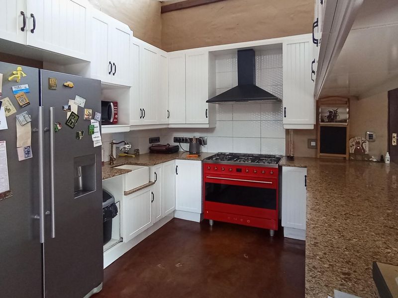 A functional kitchen featuring white cabinetry, granite countertops, a farmhouse sink, and a prominent red gas stove with an extractor fan.